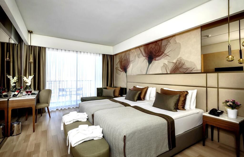 Een hotelkamer met twee bedden, een bureau met stoel, een grote spiegel en uitzicht op de omgeving.