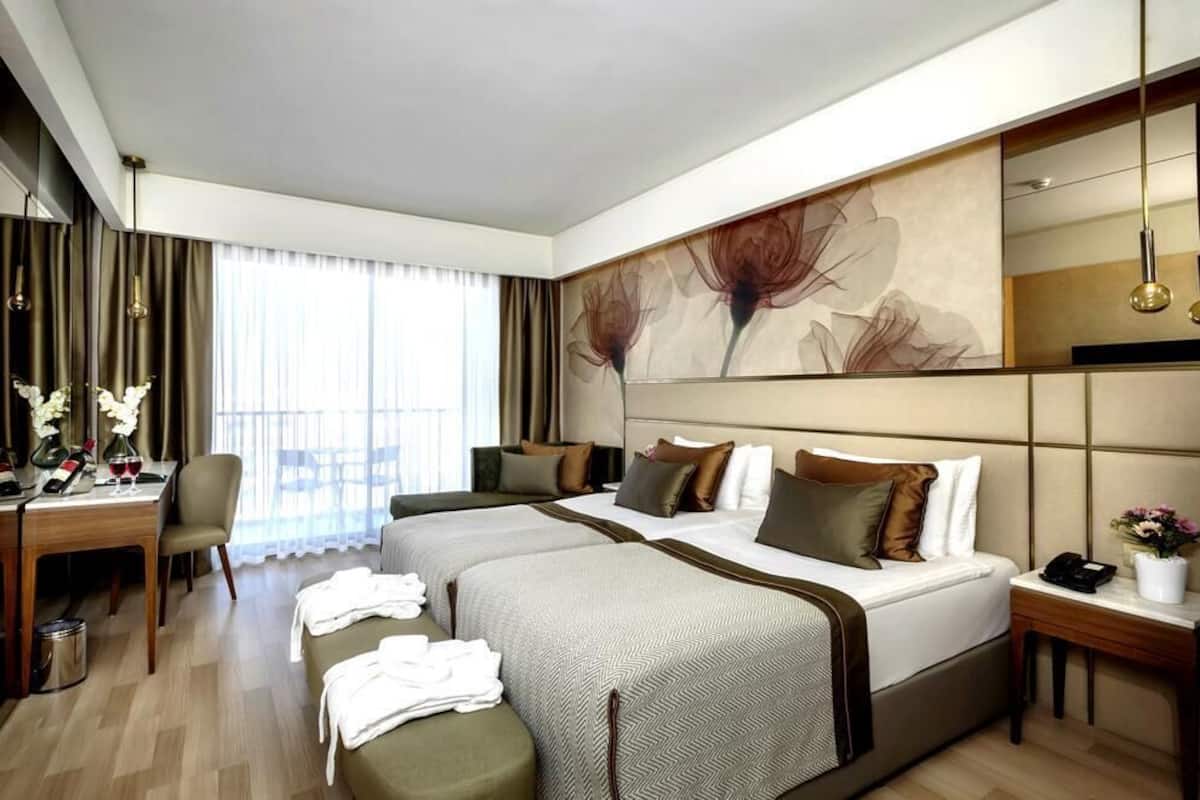 A hotel room with two beds, a desk with a chair, a large mirror, and a view of the outdoors.