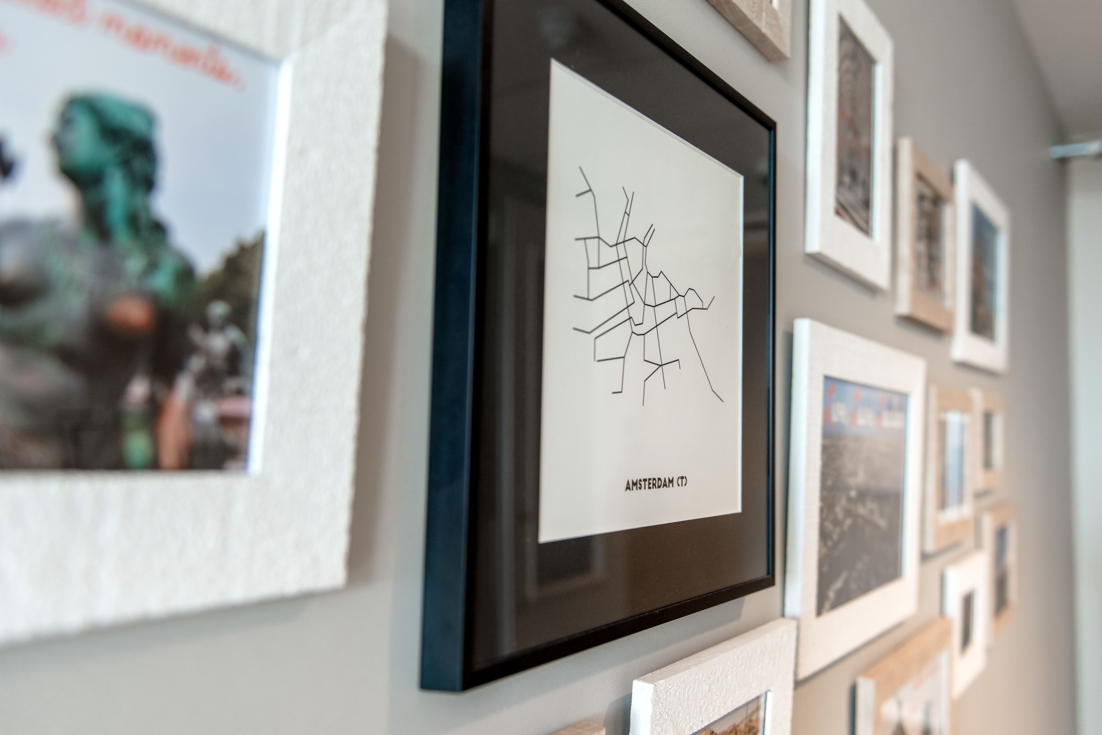 A wall with multiple framed artworks, including a map labeled "AMSTERDAM (CT)."