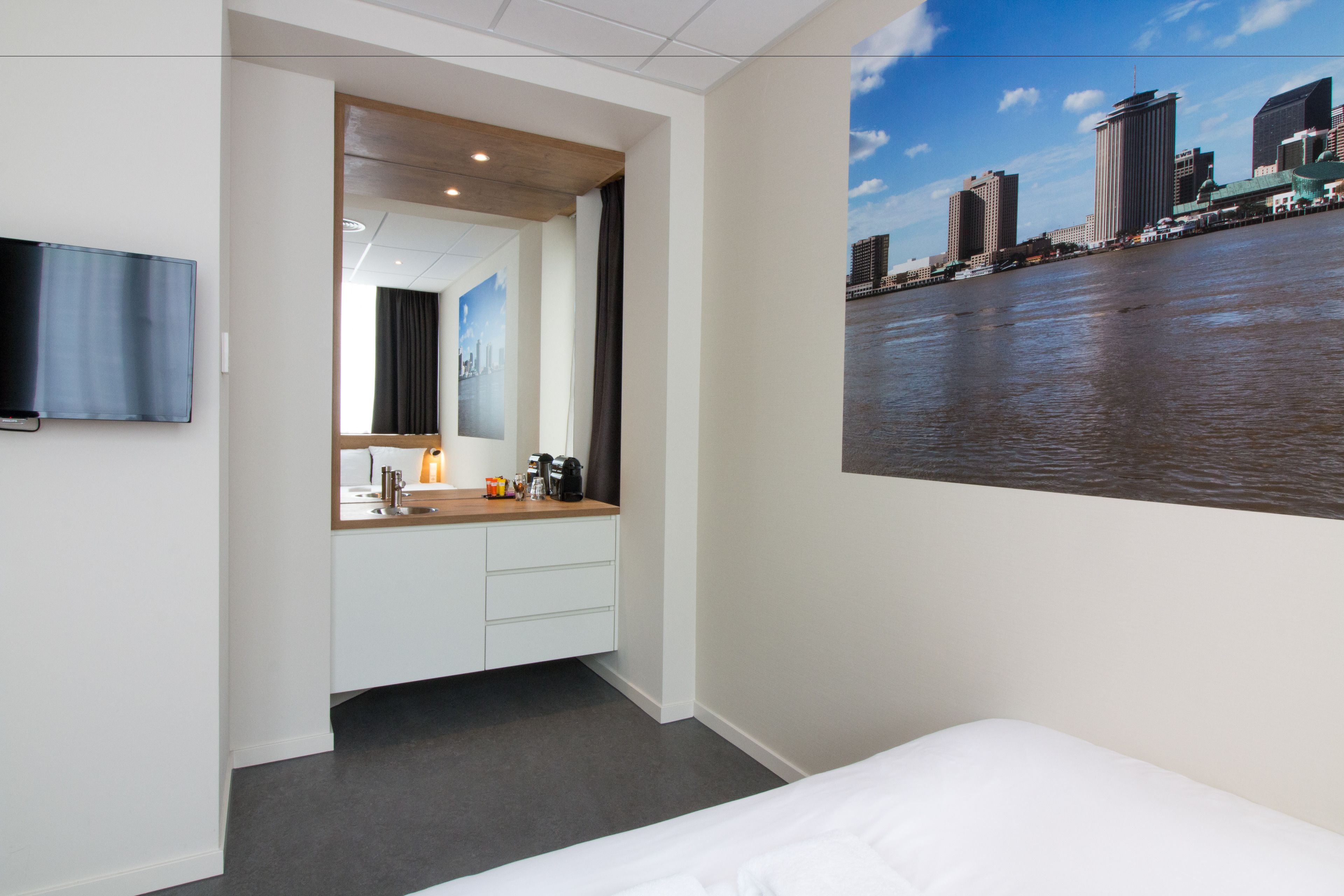 Habitación de hotel con cama, televisor en la pared, baño con espejo y vistas a la ciudad.