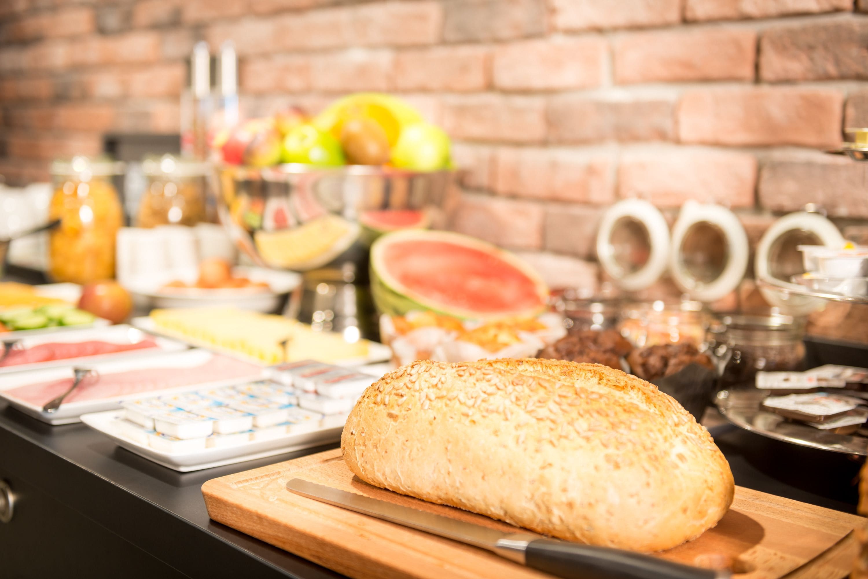 Una mesa de buffet con diversos alimentos y una hogaza de pan sobre una tabla de cortar.