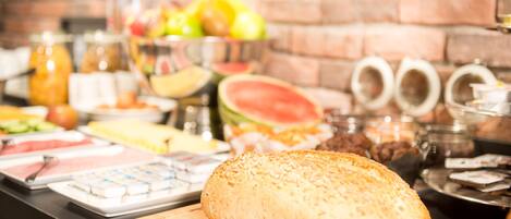 A buffet table with various food items and a loaf of bread on a cutting board.