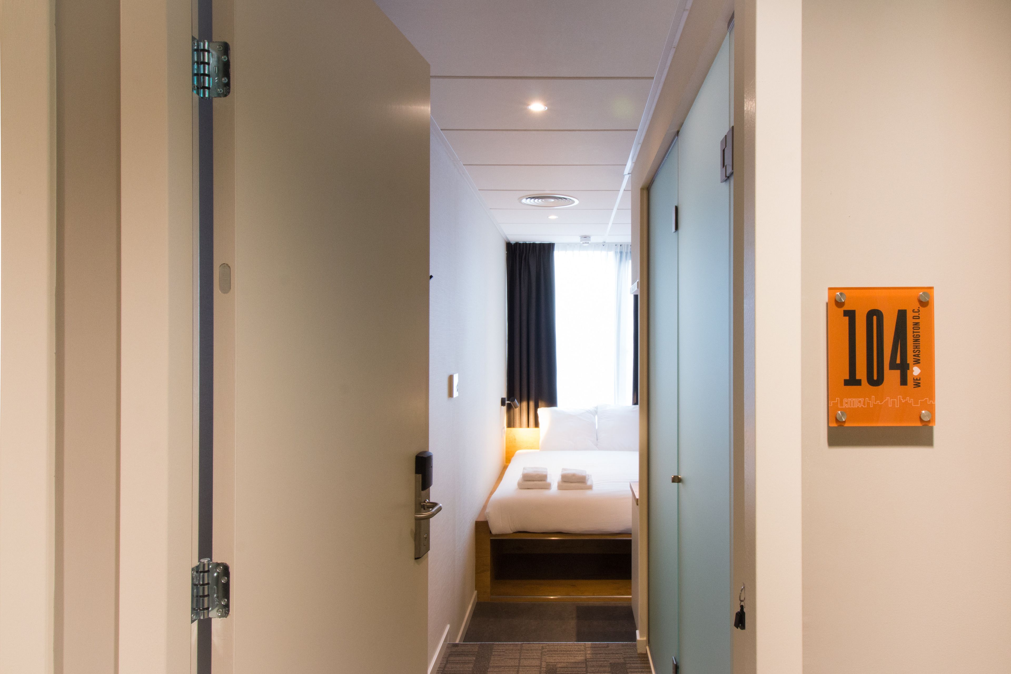 Una habitación de hotel con una cama, una mesita de noche, un teléfono en la pared y una puerta con el número.