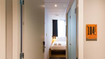 Una habitación de hotel con una cama, una mesita de noche, un teléfono en la pared y una puerta con el número.