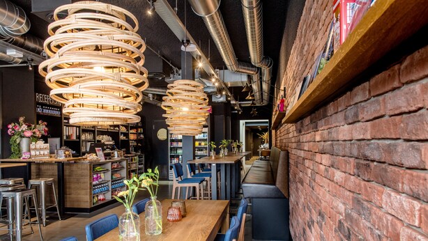 Un restaurante con una larga mesa de madera, sillas azules y lámparas colgantes de mimbre.