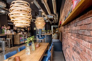 A restaurant with a long wooden table, blue chairs, and wicker pendant lights. - Citiez Hotel Amsterdam (Amsterdam)