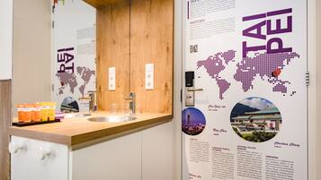 Un baño moderno con tocador de madera, un lavamanos y un espejo. Hay artículos de aseo en la encimera y un mapa de Taipéi en la pared.