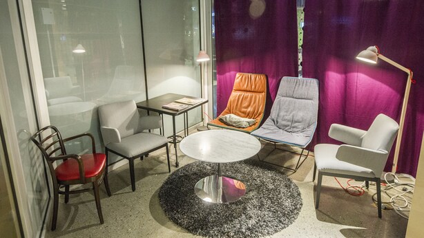 Una habitación moderna con pared de vidrio, una mesa redonda y tres sillas.