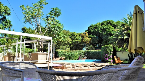Eine Terrasse mit Korbmöbeln, einem Pool und üppiger Bepflanzung.