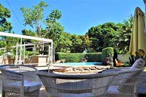 A patio area with wicker furniture, a pool, and lush greenery.