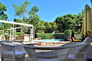 Un patio con mobiliario de mimbre, una piscina y abundante vegetación.