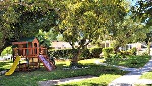 Ein Spielplatz mit Rutsche und Klettergerüst, umgeben von Gras und Bäumen.