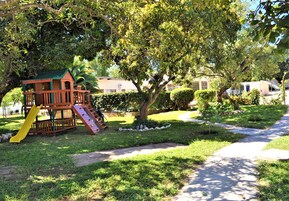 Un parque infantil con un tobogán y una estructura para escalar, rodeado de césped y árboles.