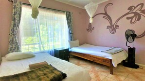 Ein Zimmer mit zwei Betten, einem Moskitonetz, einem Ventilator und einem fenster mit Vorhängen.