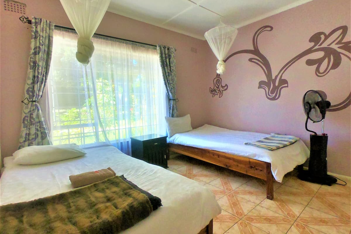 Une chambre avec deux lits, une moustiquaire, un ventilateur et une fenêtre avec des rideaux.