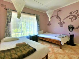Una habitación con dos camas, mosquitero, ventilador y ventana con cortinas.