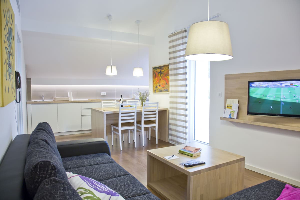 A modern living room with a sofa, a coffee table, and a TV. There is a dining area with a table and chairs in the background.