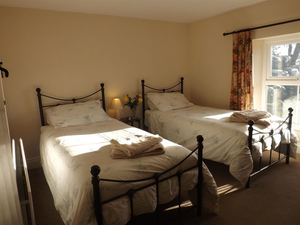 A bedroom with two single beds, a bedside table with a lamp, and a window with curtains.
