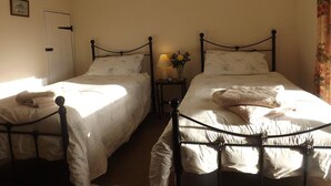 A bedroom with two single beds, a bedside table with a lamp, and a door. - Hillis Close Farm (Haltwhistle)