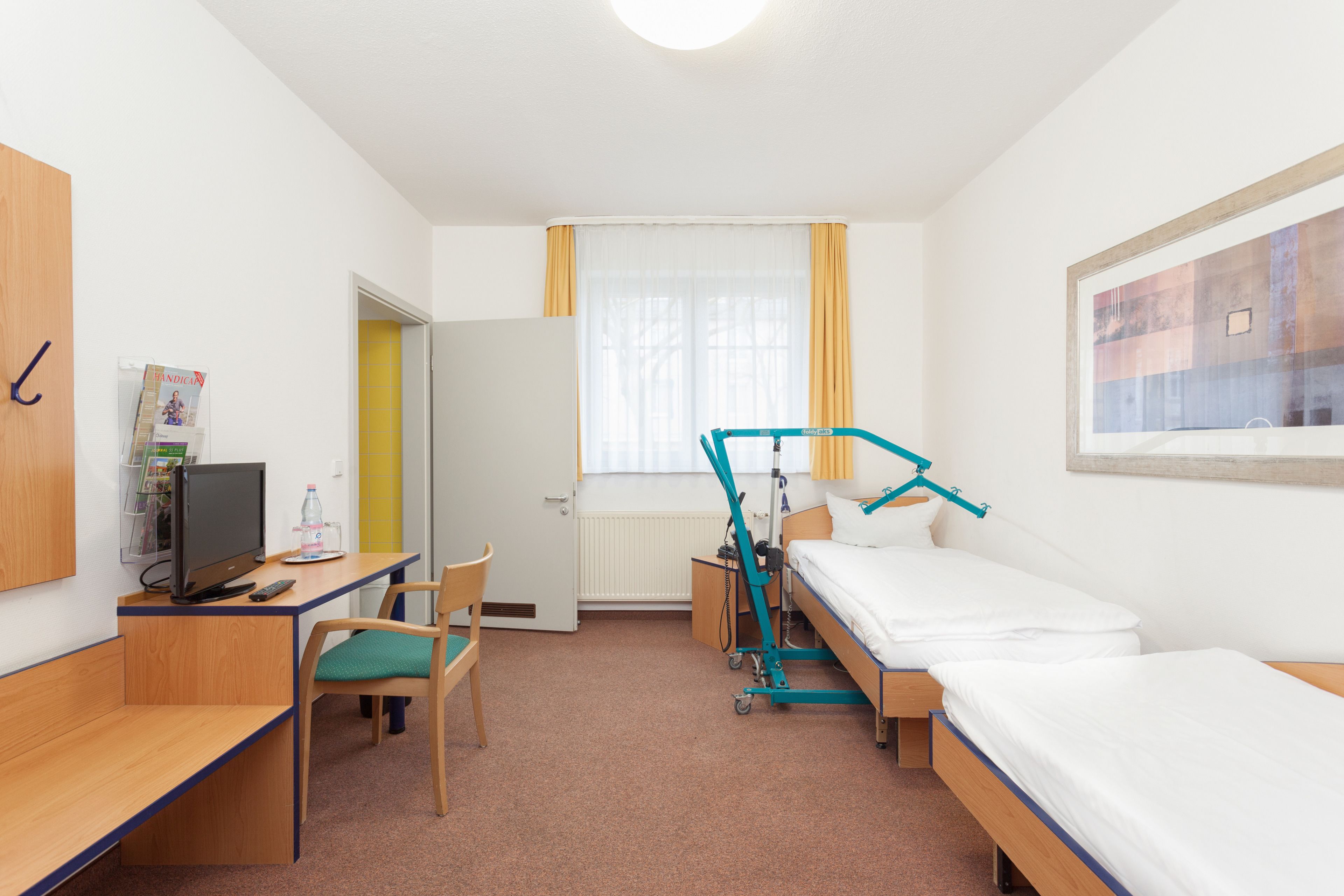 Habitación de hotel con cama, escritorio, silla, televisión y ventana con cortinas.