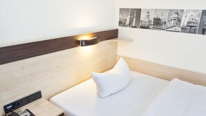 Una habitación de hotel con una cama bien hecha, un teléfono en la mesita de noche y una lámpara de pared.