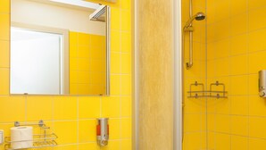 Un baño con pared de azulejos amarillos, un lavamanos blanco y una zona de ducha.