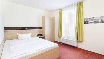 Quarto de hotel com cama, mesa de cabeceira, guarda-roupa e janela com cortinas.