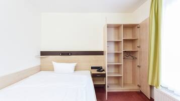 A hotel room with a bed, a wooden wardrobe, a nightstand, and a radiator.