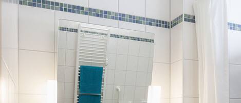 Un baño con lavamanos blanco, encimera con motas azules y espejo con resalte de azulejos azules.