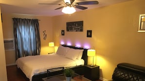 A hotel room with a bed, bedside lamps, a ceiling fan, a small table with a plant, a couch, and a window with curtains. - Delux Inn Clearwater (Clearwater)