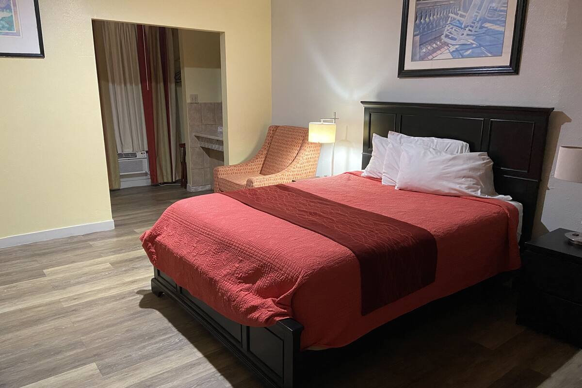 A hotel room with a bed, a chair, a nightstand, and a lamp.