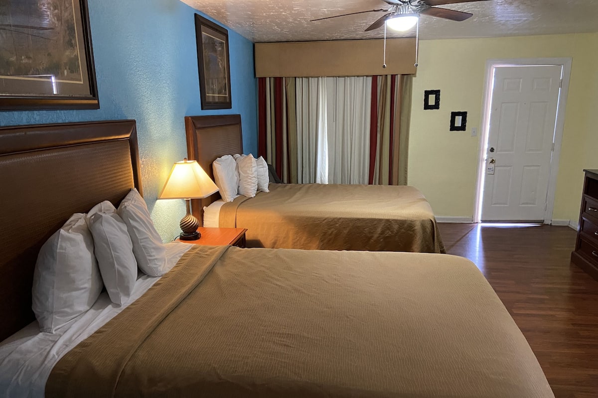 A hotel room with two beds, a ceiling fan, a lamp, and a door.