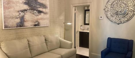 A beige sofa, a blue armchair, a large abstract painting, and a decorative metal piece on the wall.
