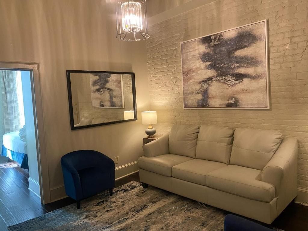 A room with a beige sofa, a blue armchair, a mirror, a lamp, and abstract art on the wall.