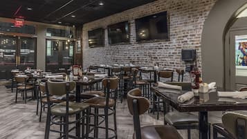 A restaurant with brick walls, multiple tables and chairs, and a television mounted on the wall.
