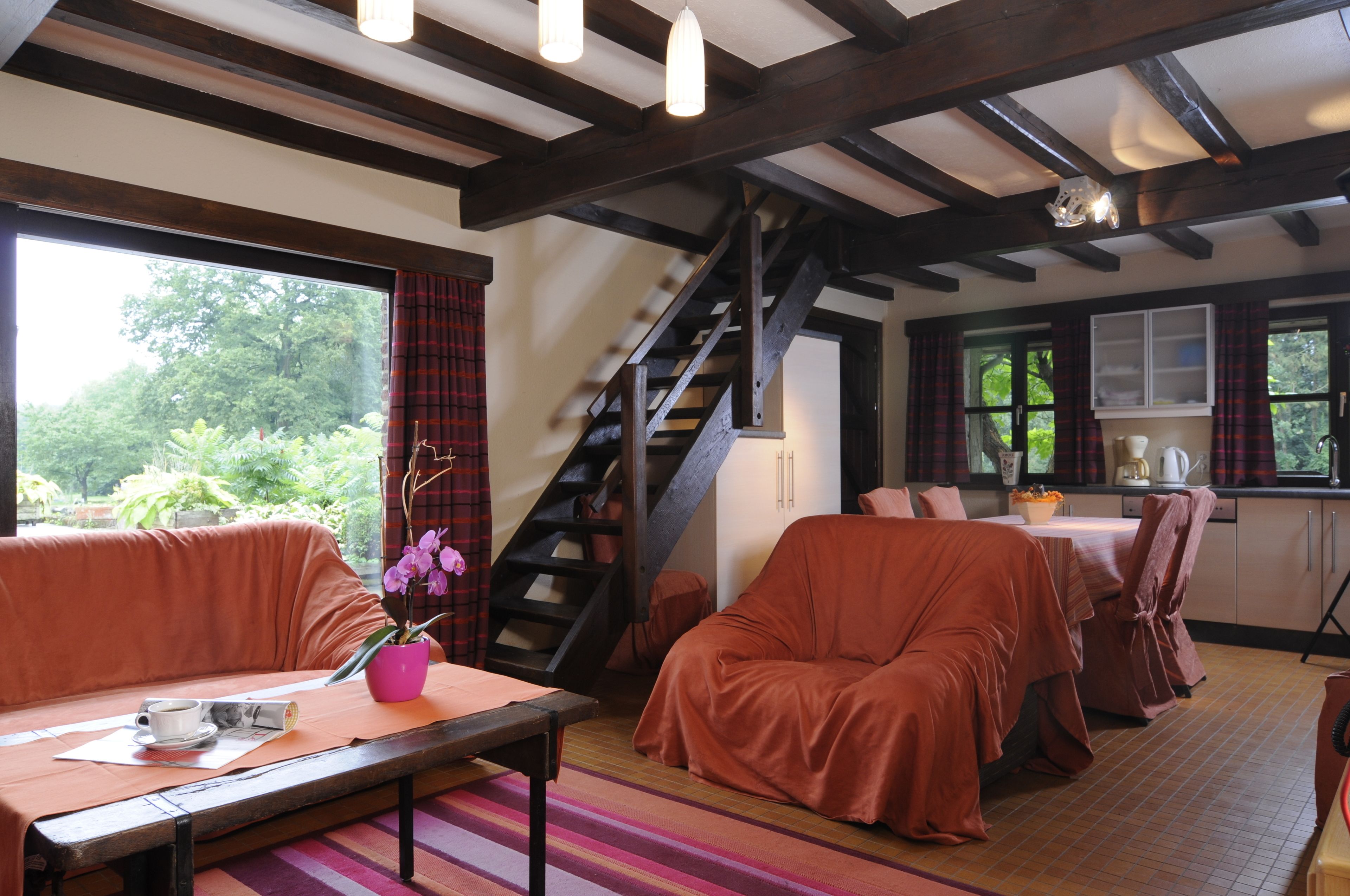 A cozy room with a wooden staircase, a dining area, and a seating area with a table and chairs.