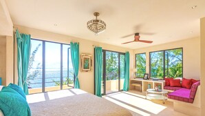A bedroom with a large bed, a desk, a sofa, and a view of the ocean. - Villa Encantada by Coco B Isla (Isla Mujeres)