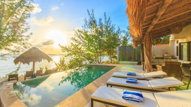 A poolside area with lounge chairs and a thatched roof structure. - Villa Encantada by Coco B Isla (Isla Mujeres)