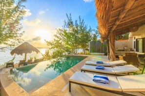 Un espace aménagé au bord de la piscine, avec des chaises longues et une structure dotée d’un toit en chaume.