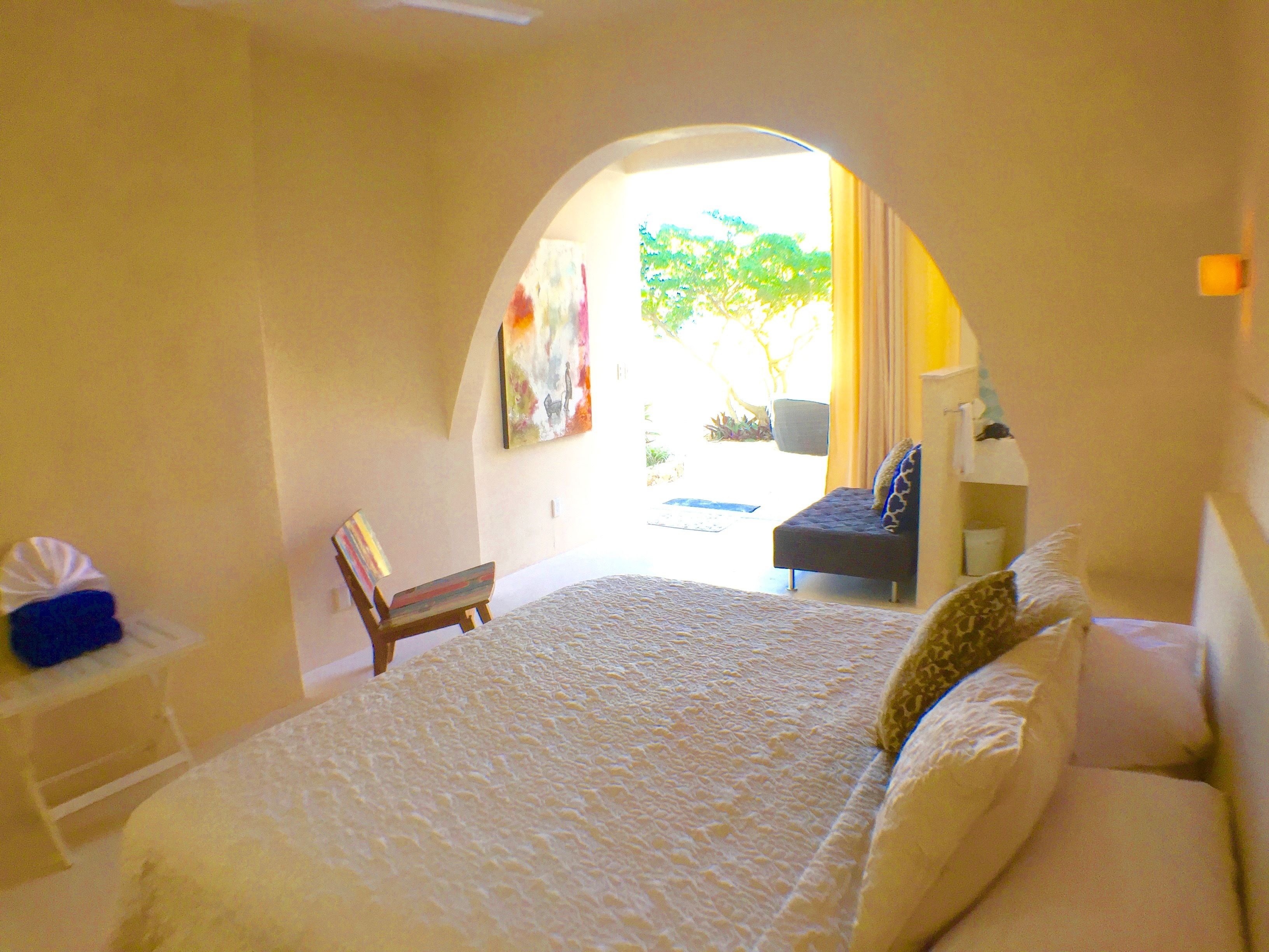 A bedroom with a large bed, a chair, a desk, and a painting on the wall.