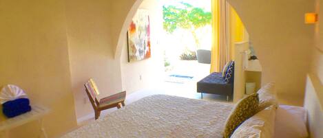 A bedroom with a large bed, a chair, a desk, and a painting on the wall.