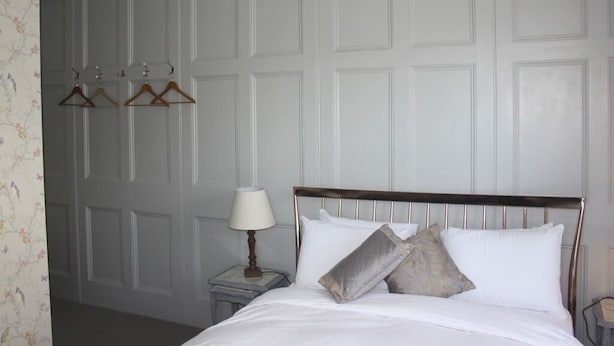 A neatly made bed with a wooden headboard, a bedside lamp, and three wooden hangers on a wall-mounted rack. - Portreath Arms (Redruth)