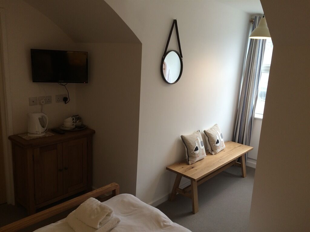 A hotel room with a bed, a wooden bench, a television, a mirror, and a window with curtains.