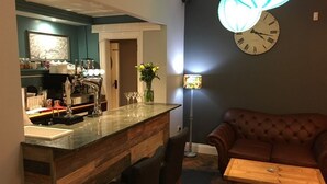 A kitchen with a wooden bar, a coffee machine, and a vase with flowers. There is a brown leather couch and a wooden table in the living area. - Portreath Arms (Redruth)