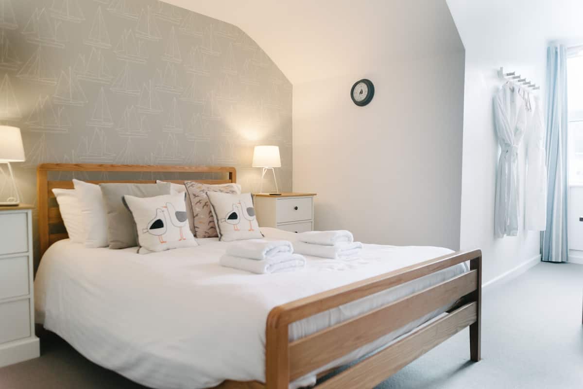 A neatly made bed with white linens and decorative pillows, a wooden headboard, bedside lamps, and a wall clock.