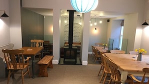 A dining area with wooden tables and chairs, a stone wall, and a hanging light fixture. - Portreath Arms (Redruth)