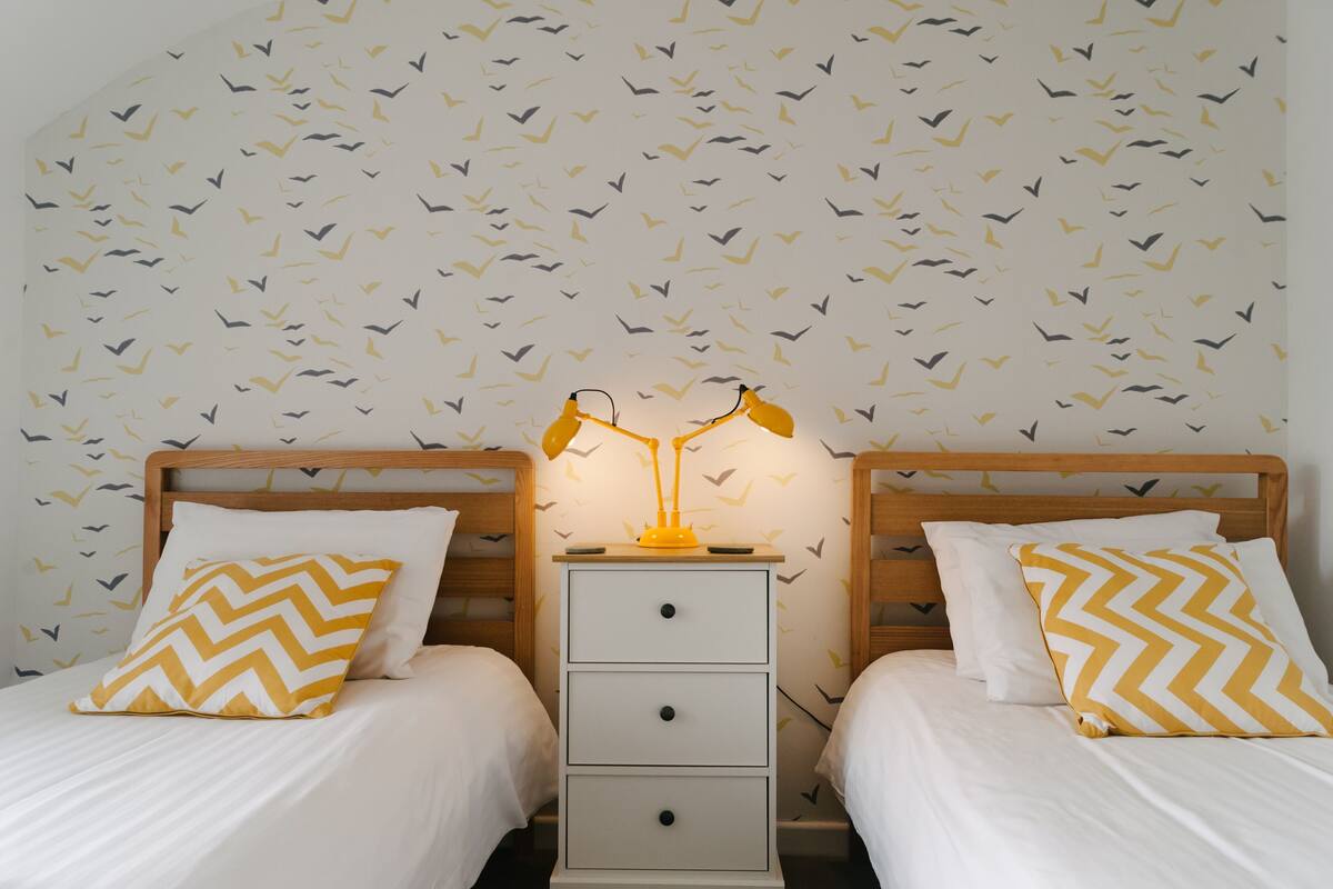 A double bed with two nightstands, each with a lamp, and a wall with a bird pattern.