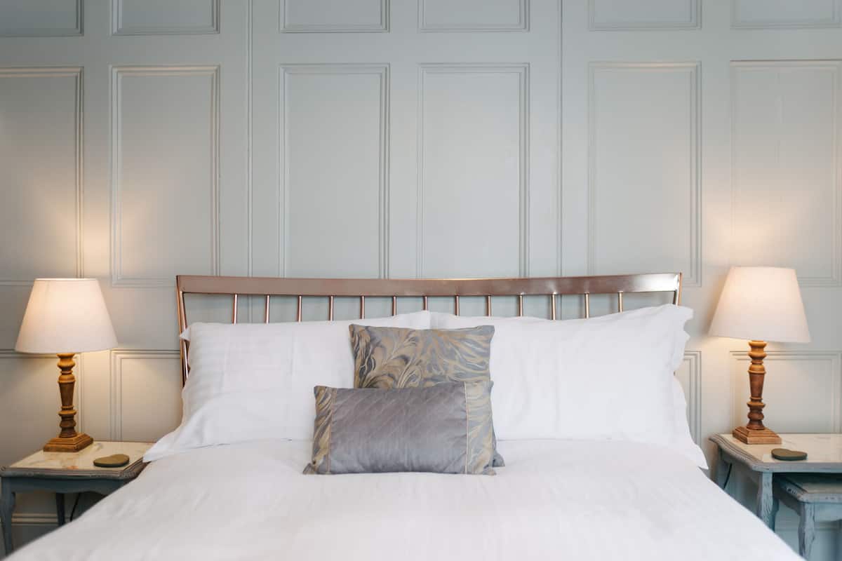 A neatly made bed with white linens and two decorative pillows, flanked by two bedside tables with lamps.