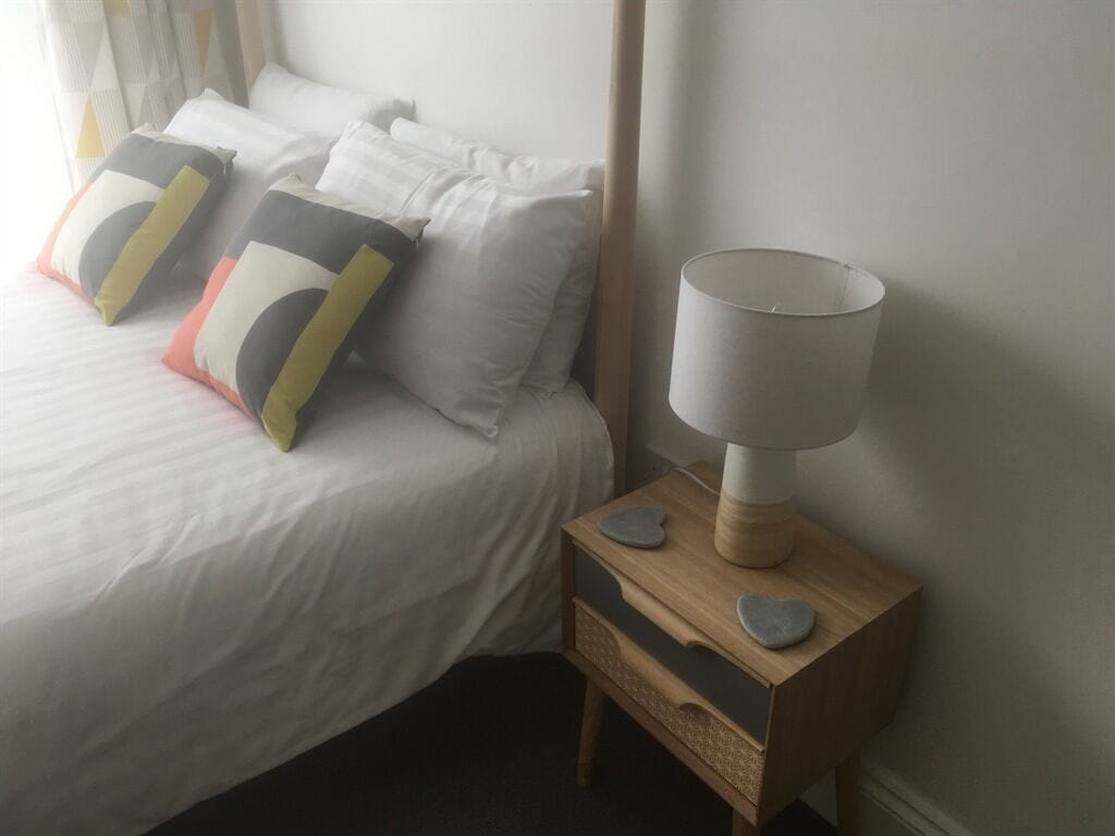 A neatly made bed with pillows, a bedside lamp, and a wooden nightstand with drawers.