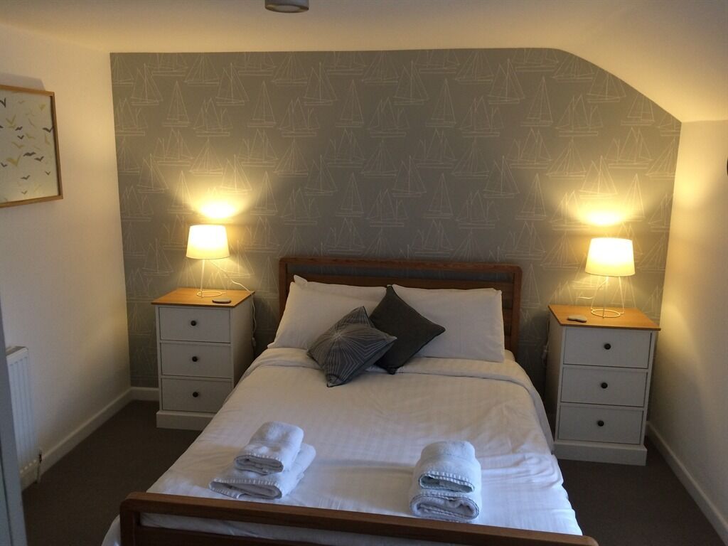 Un lit bien fait, avec deux oreillers, deux tables de chevet dotées de lampes et un mur orné d’un motif.